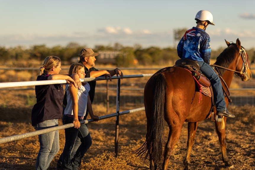 Keluarga berdiri di pagar menonton anak laki-laki menunggang kuda