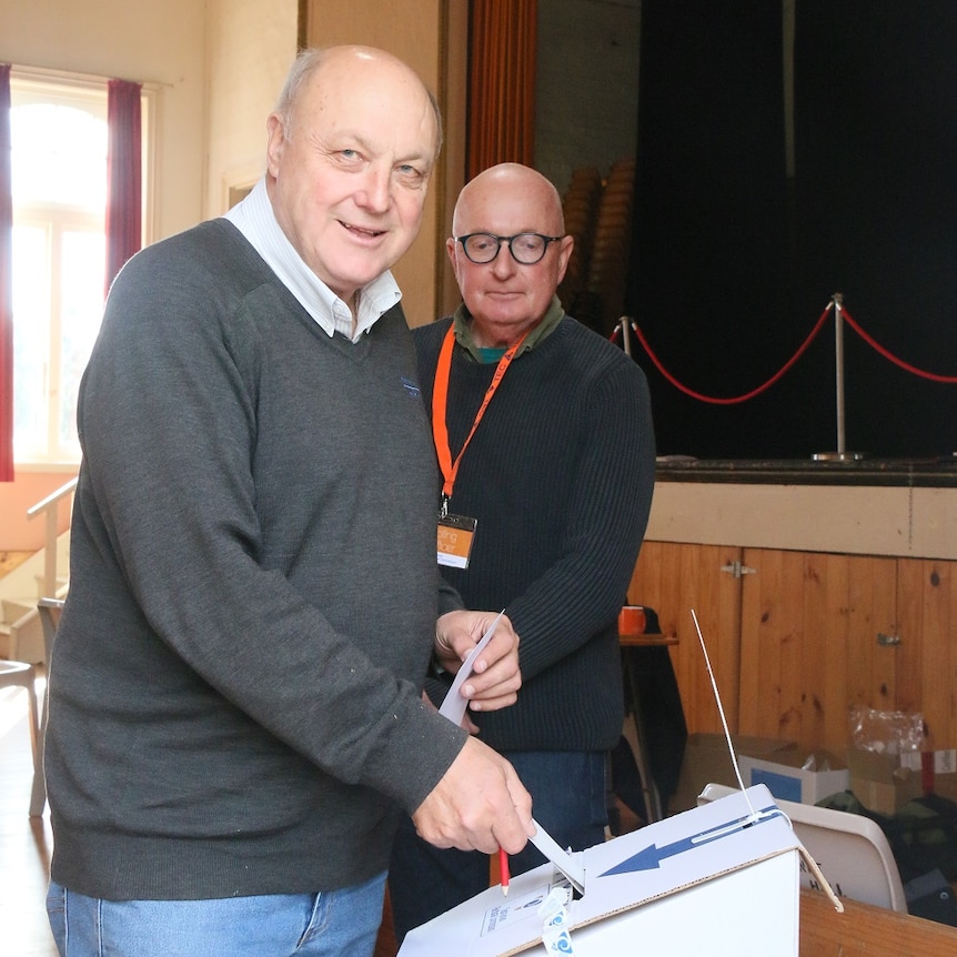 Man puts a ballot paper in the ballot box as an Electoral Commission official watches on