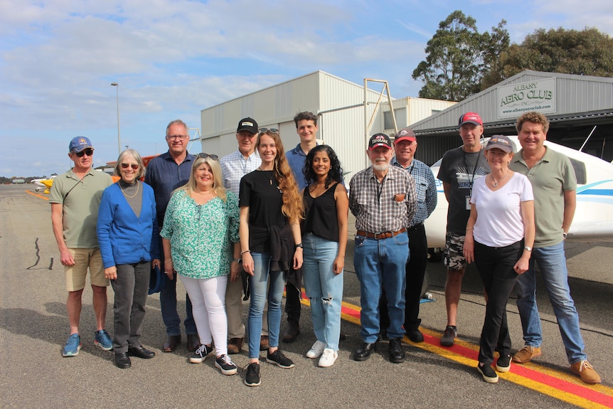 A group stand in front of a plane on the tarmac