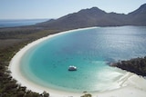 View of a curved bay with bright blue water, white sand and green trees behind the beach