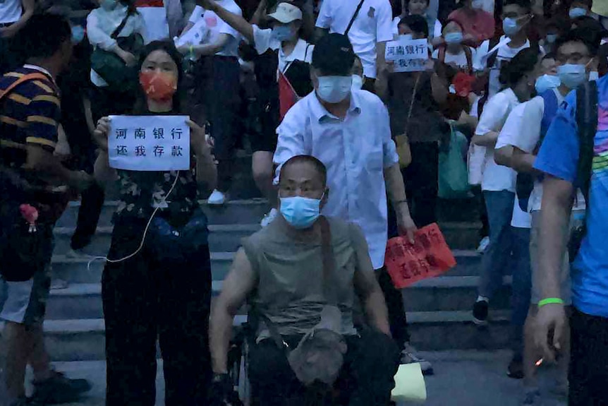 A man in a wheelchair is next to a woman holding a sign