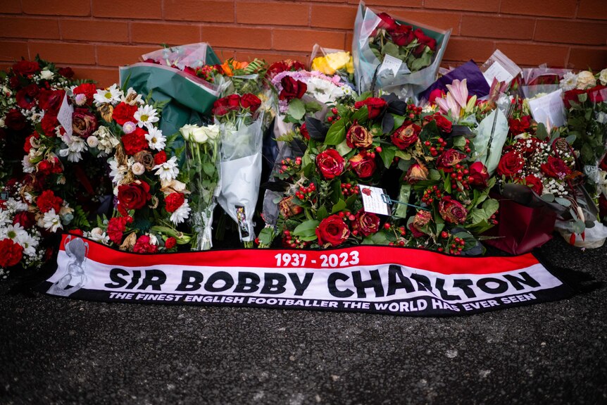 Flowers lie above a red and white scarf that reads SIR BOBBY CHARLTON