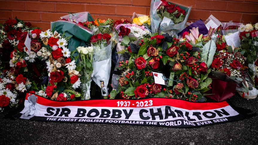 Flowers lie above a red and white scarf that reads SIR BOBBY CHARLTON