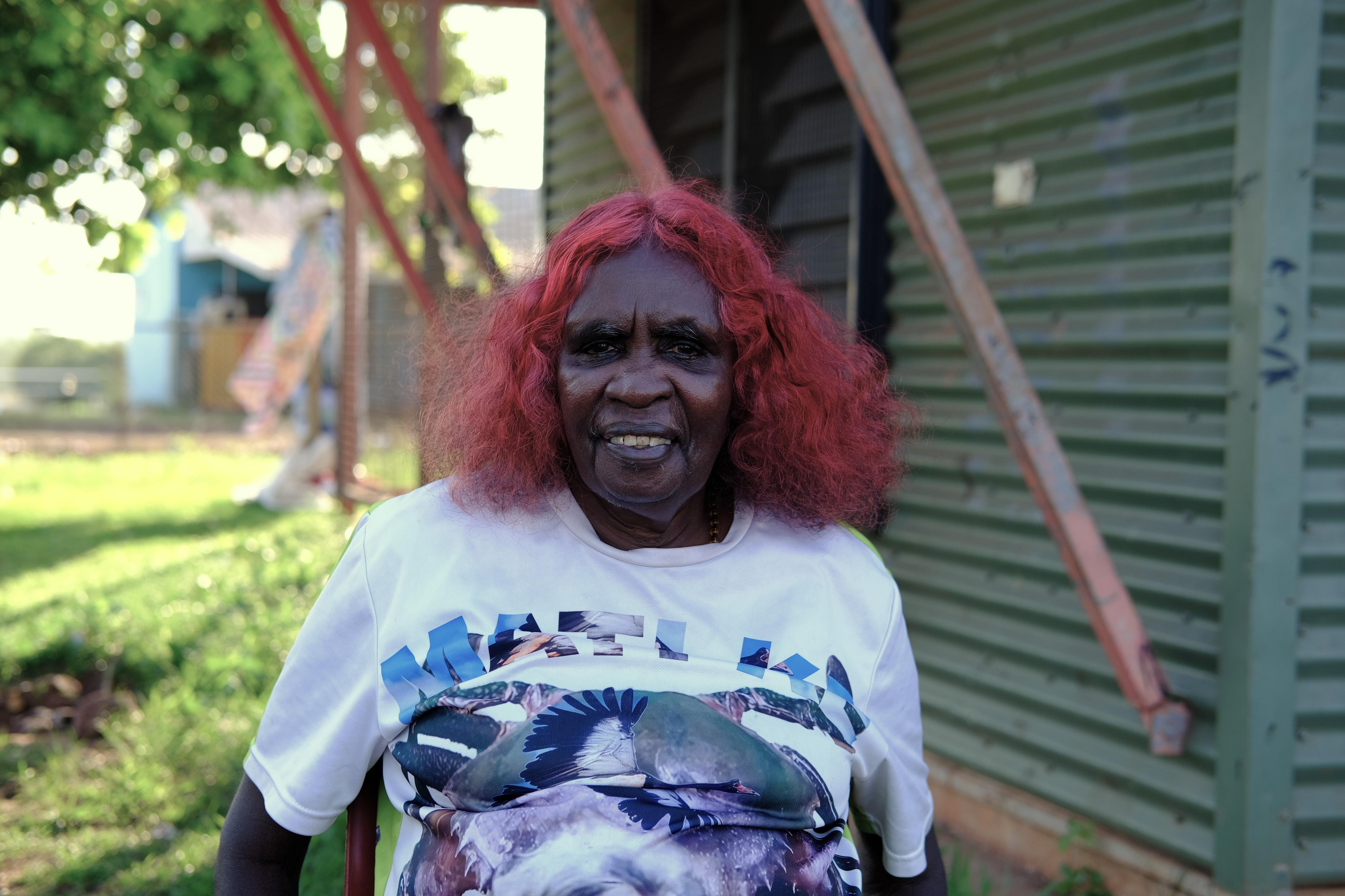 Margaret Perdjert smiles for the camera while sitting outdoors with her hair dyed a vibrant red.