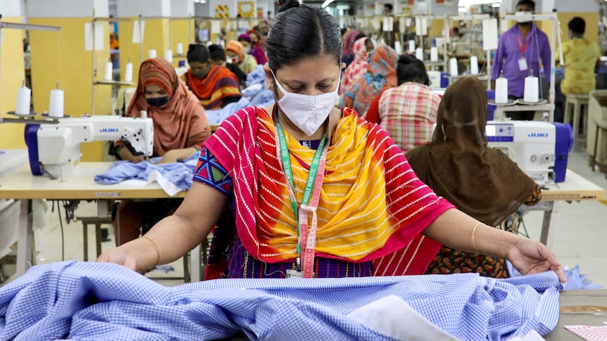 A woman in a face mask looking at fabric in a garment factory