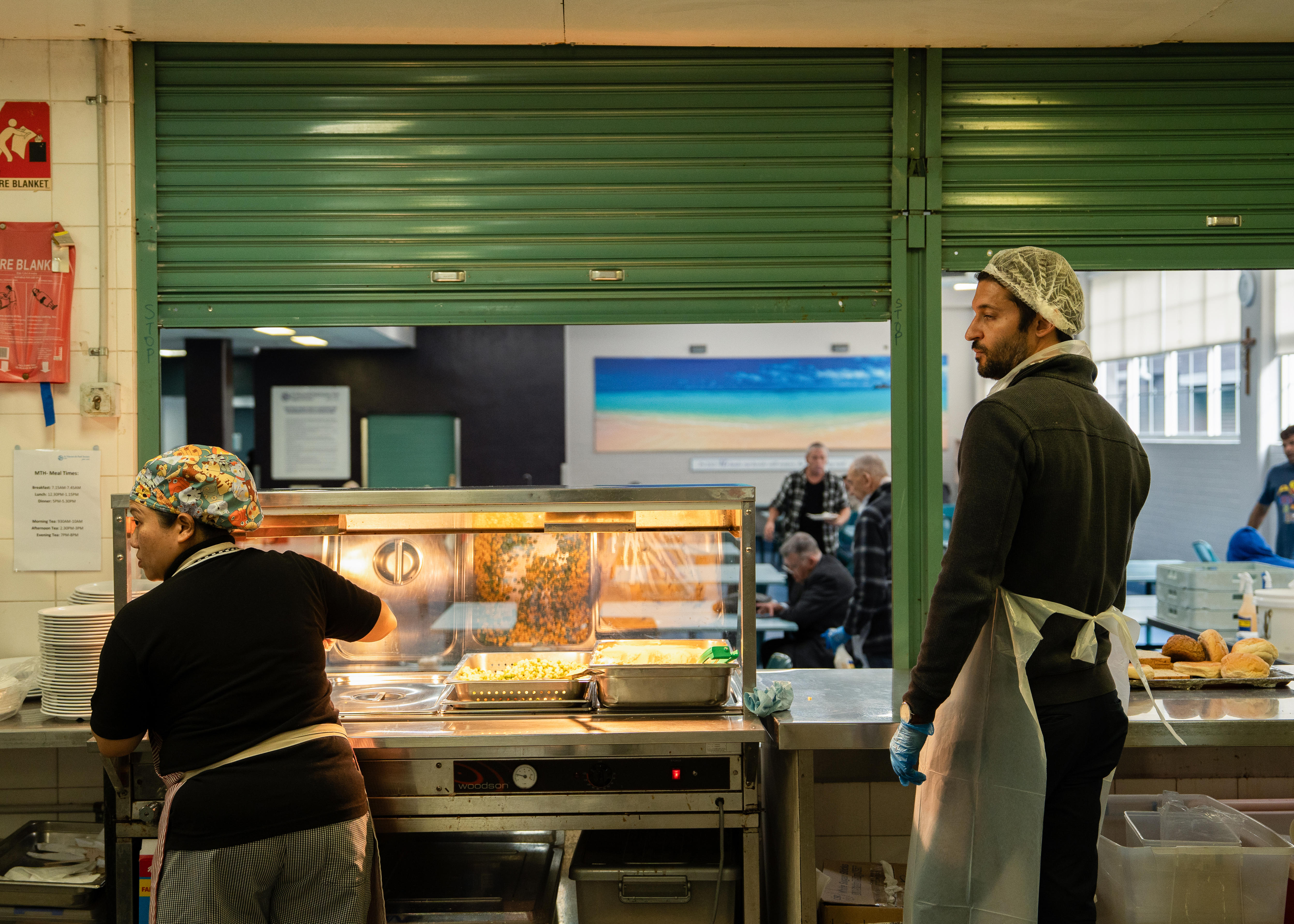 A woman and man stand in the kitchen of a hostel for homeless men.