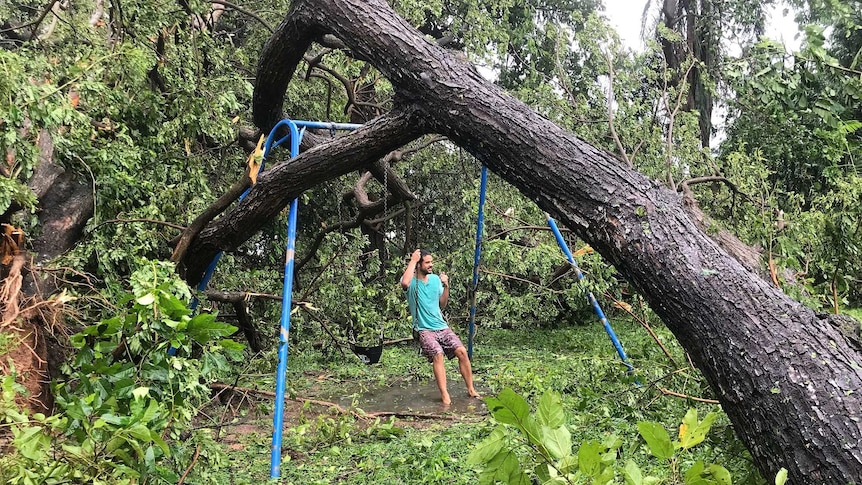 A man swings on a swingset pinned by a fallen tree in Darwin after Cyclone Marcus.