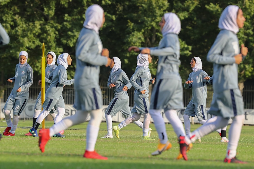 women soccer players wearing grey uniforms and hijabs warm up