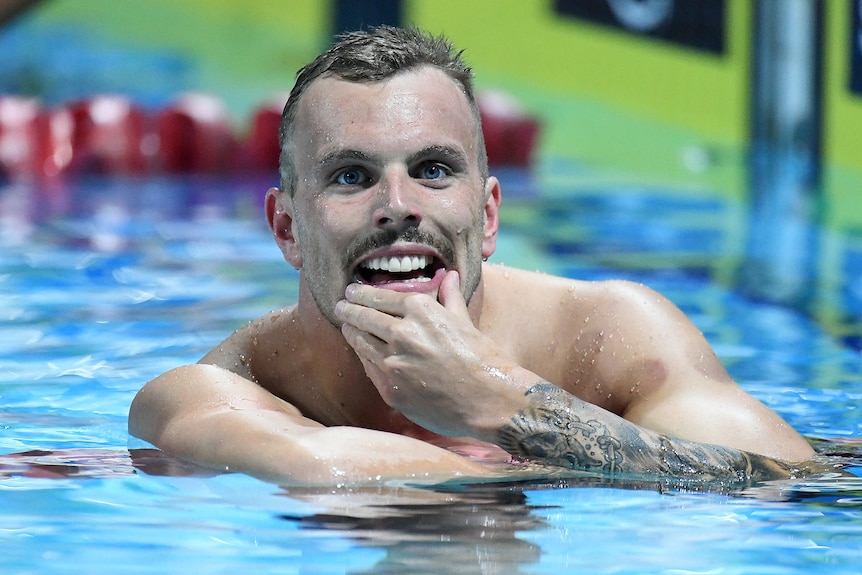 Kyle Chalmers smiles and touches his chin as he rests on a lane rope after a race.