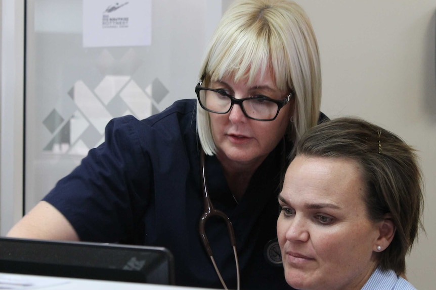 Shiree points at the screen in reception with a female receptionist