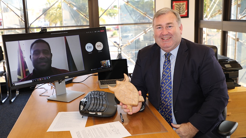 a man sits at a desk in front of a computer, holding a wooden turtle