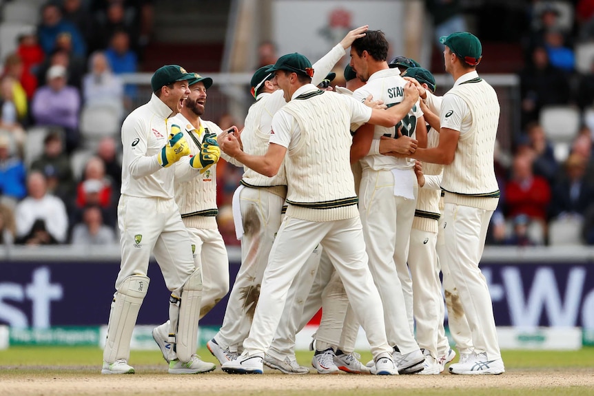 The Australian team celebrates a wicket in a huddle.