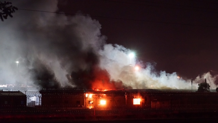 Grey clouds of what looks like smoke billows from a building that appears to be on fire.