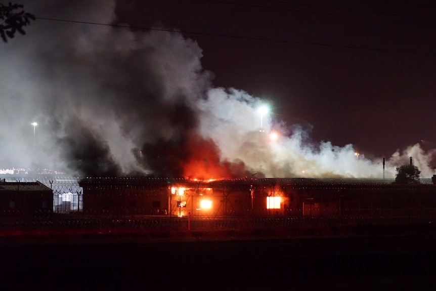 Grey clouds of what looks like smoke billows from a building that appears to be on fire.