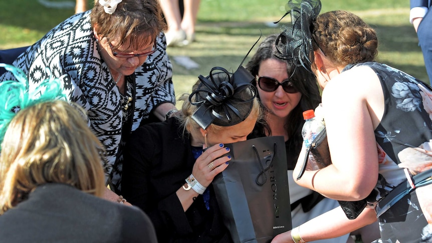 A punter appearing to vomit into bag at the Melbourne Cup.