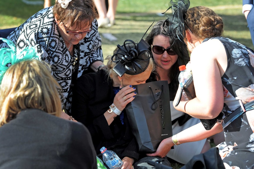 A punter appearing to vomit into bag at the Melbourne Cup.