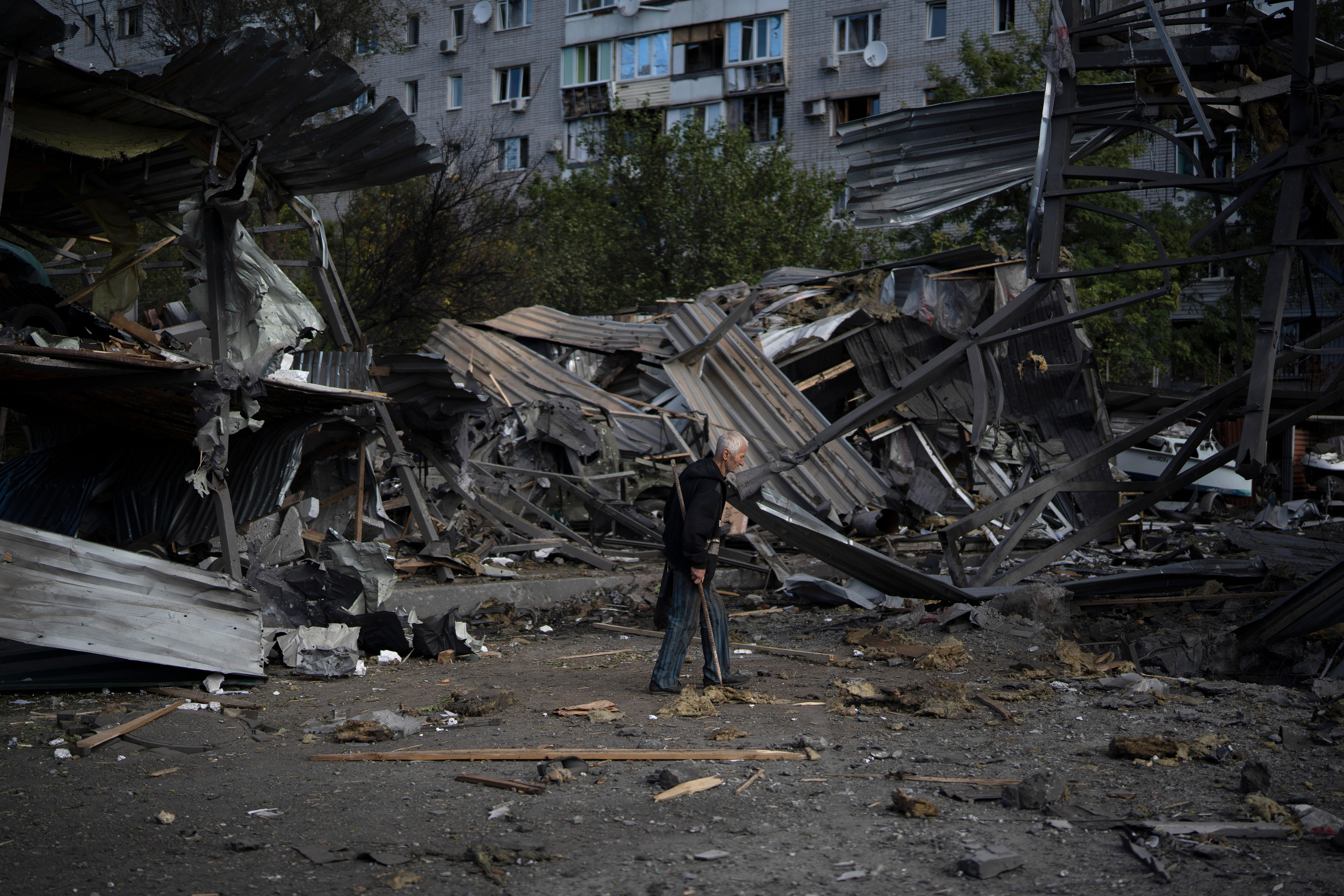 An elderly man walks past sheet metal wreckage of a former car shop.