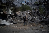 An elderly man walks past sheet metal wreckage of a former car shop.