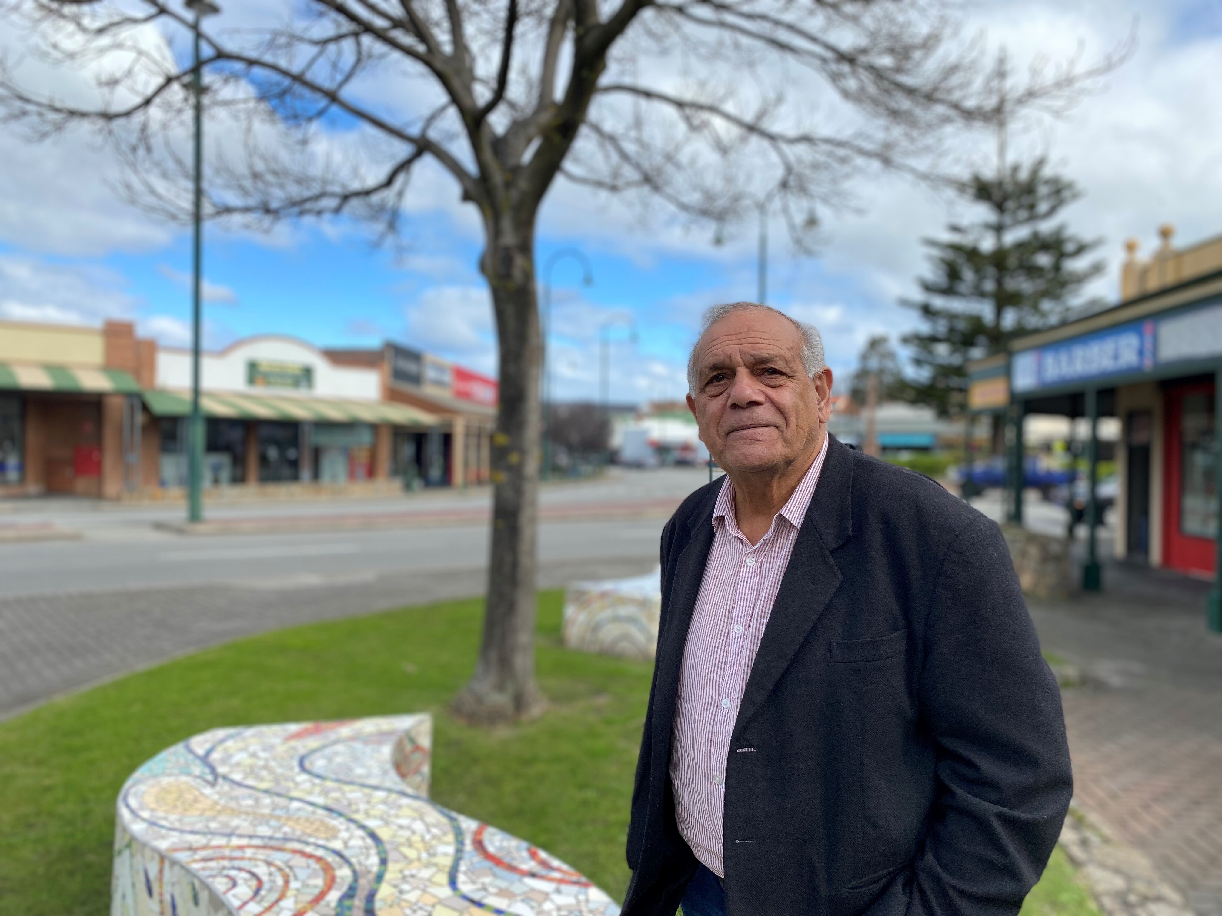 An Indigenous man wearing a suit stands in the street next to a tree.