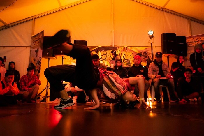 A crowd watch a breakdancer bending backwards over the floor.