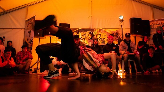 A crowd watch a breakdancer bending backwards over the floor.