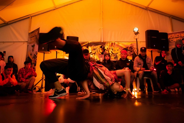 A crowd watch a breakdancer bending backwards over the floor.