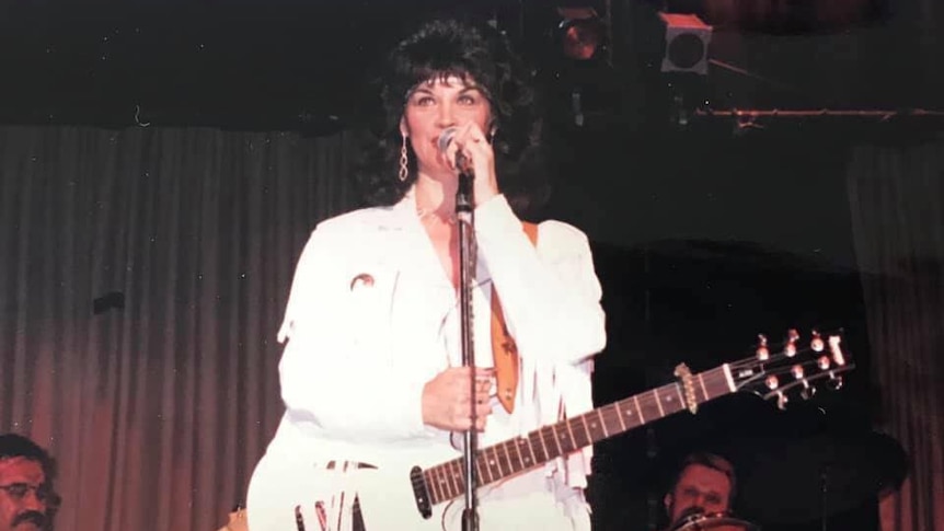 A woman in an all-white outfit playing guitar and singing on stage
