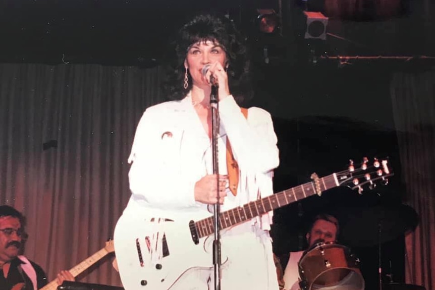 A woman in an all-white outfit playing guitar and singing on stage