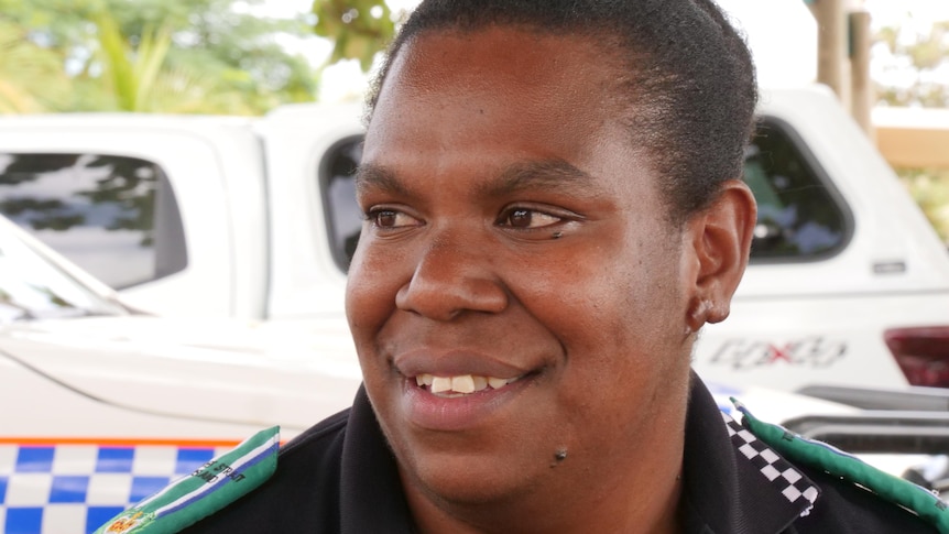 A woman in police liaison uniform with police cars behind her