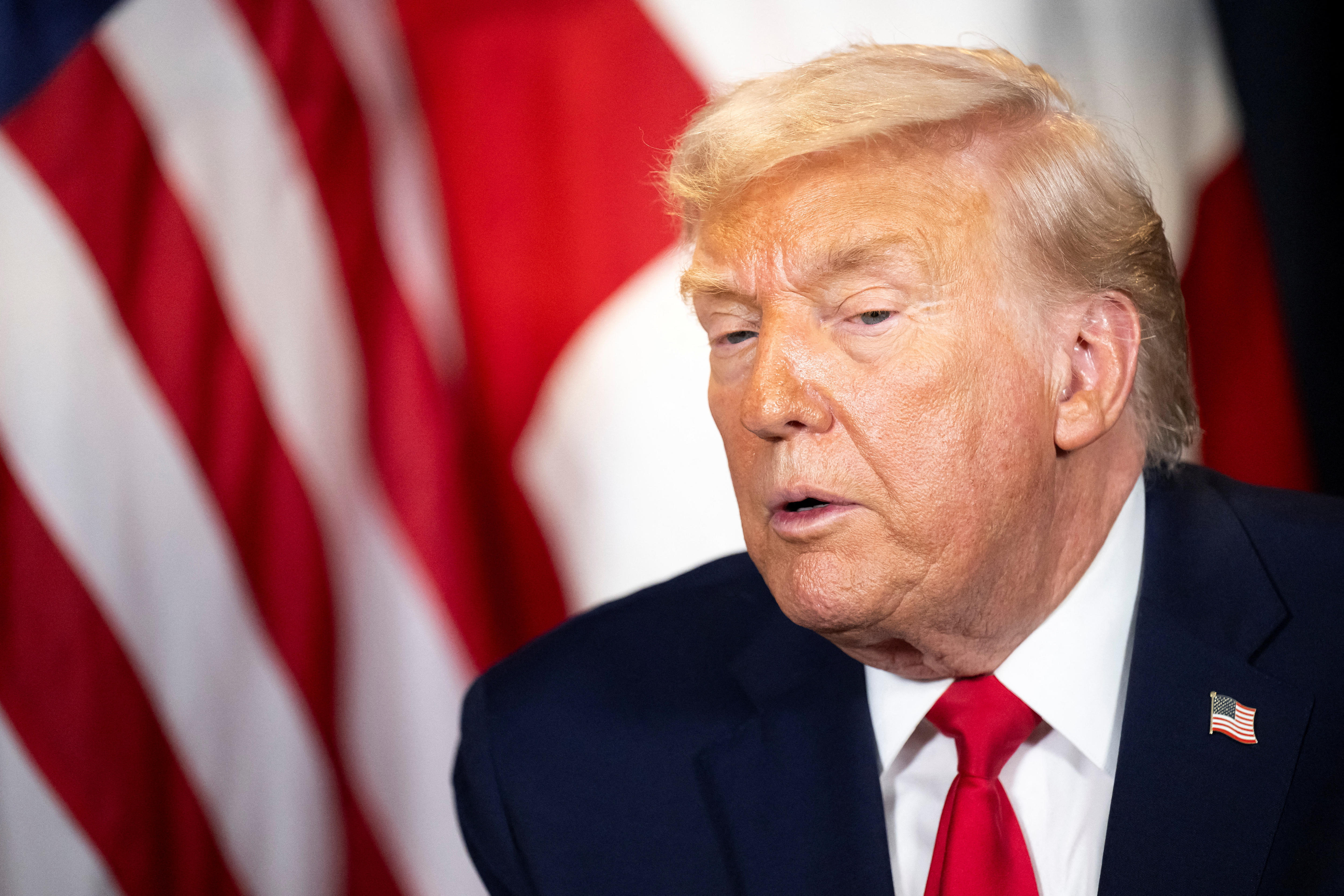 Donald Trump leans over as he stands at a podium in front of a united States flag