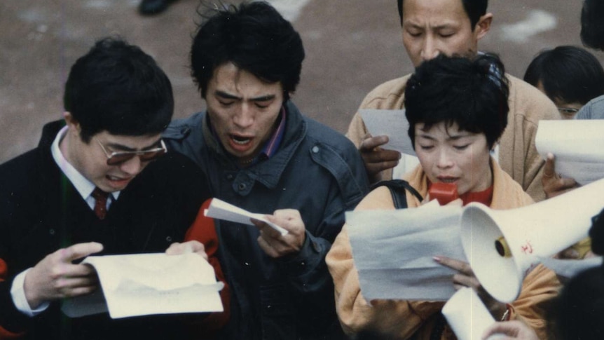 You see a scanned film photo showing a group of young Chines men and women holding paper and megaphones.