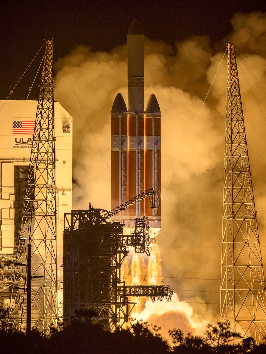 A launching rocket is seen surrounded by its support gantries and exhaust smoke.