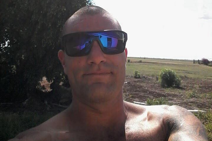 Ahead and shoulders selfie of a shirtless man wearing sunglasses in a paddock.