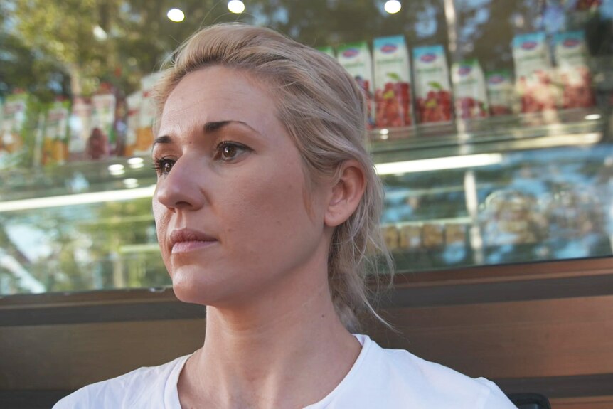 A woman wearing a white t-shirt sits outside a cafe.