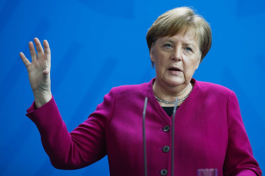Angela Merkel gestures with her hand while speaking, wearing a pink jacket.