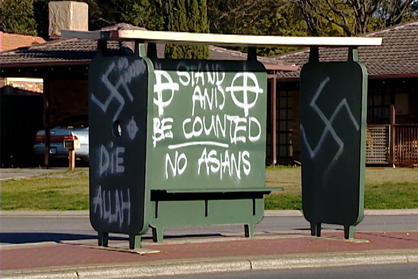 A green bus stop covered in racist and neo-Nazi graffiti.