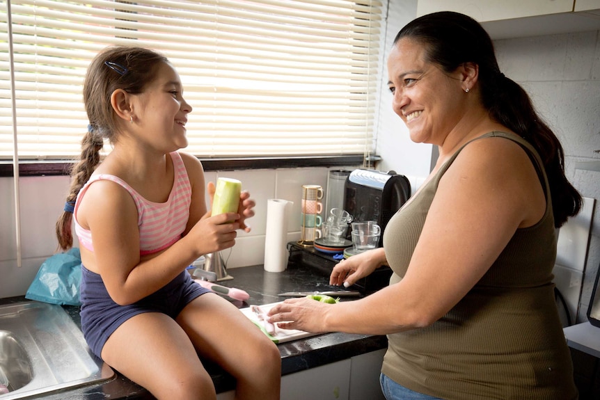 Karla De Lautour and her mother looking at each other and laughing. Karla sits on the kitchen bench, her mother stands.