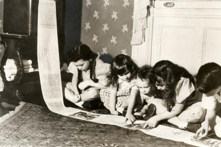Children kneel over a newspaper being pulled from a fax machine