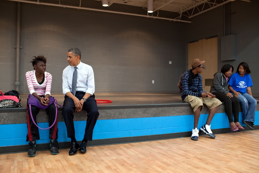 Barack Obama sits and speaks to a young girl. 