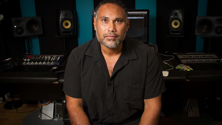 Musician in a recording studio seated in front of a mixing desk.