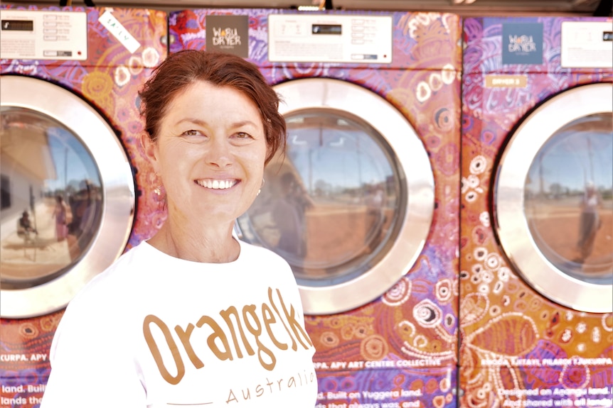 A woman in a white t shirt in front of three washing machines 