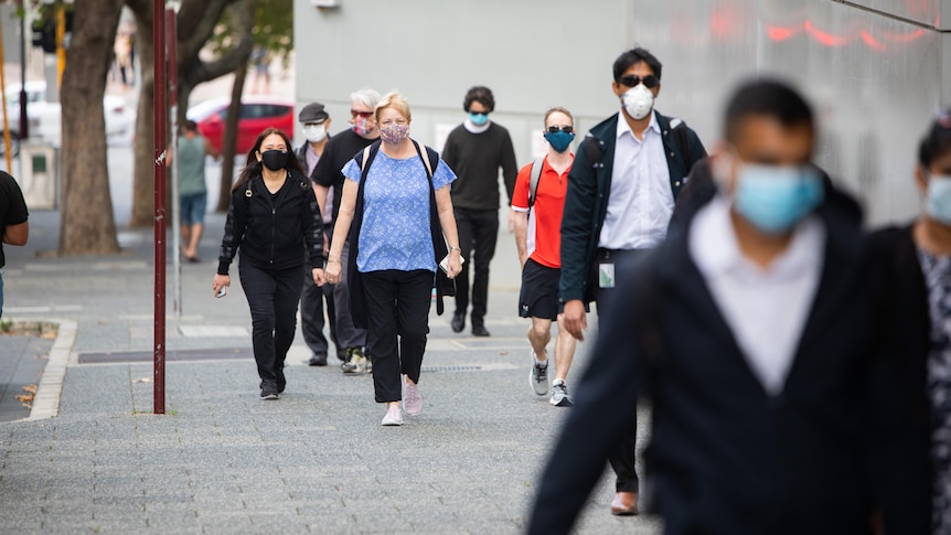 People in masks walk down a city street footpath