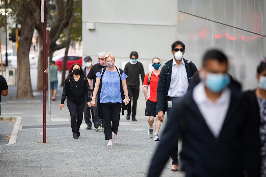 People in masks walk down a city street footpath