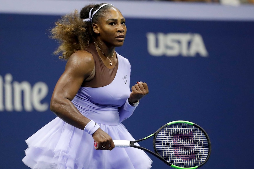 A female tennis player clenches her fist and looks into the distance wearing a purple tutu.