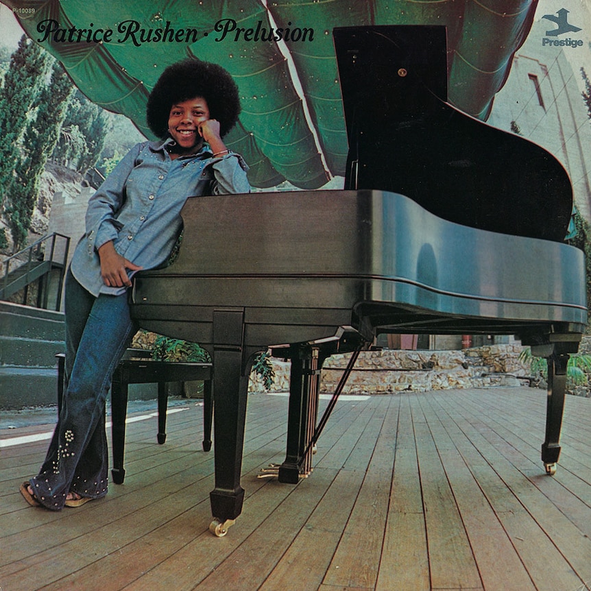 A photo of a young Patrice Rushen sporting an afro and standing on-stage, leading against a grand piano