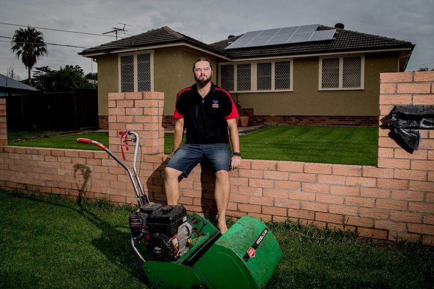 Nathan Clissold sits on his fence near his mower.