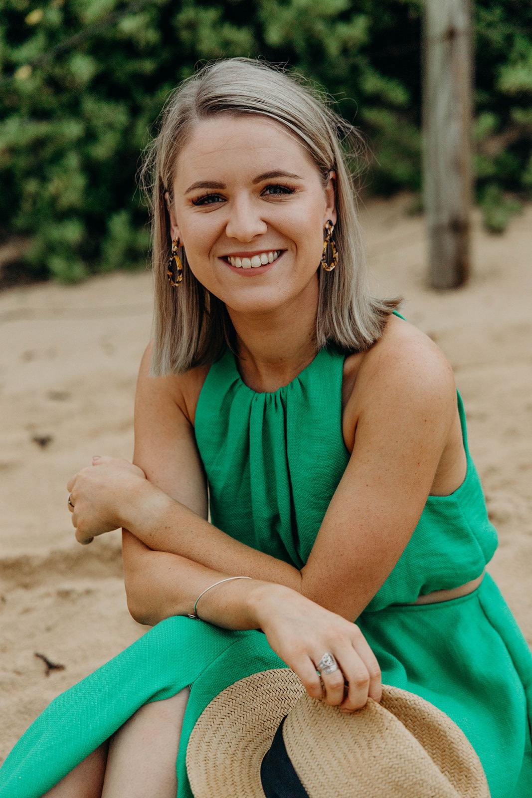 Lacinda Fisk sits outside in a green dress, holding a hat and smiling