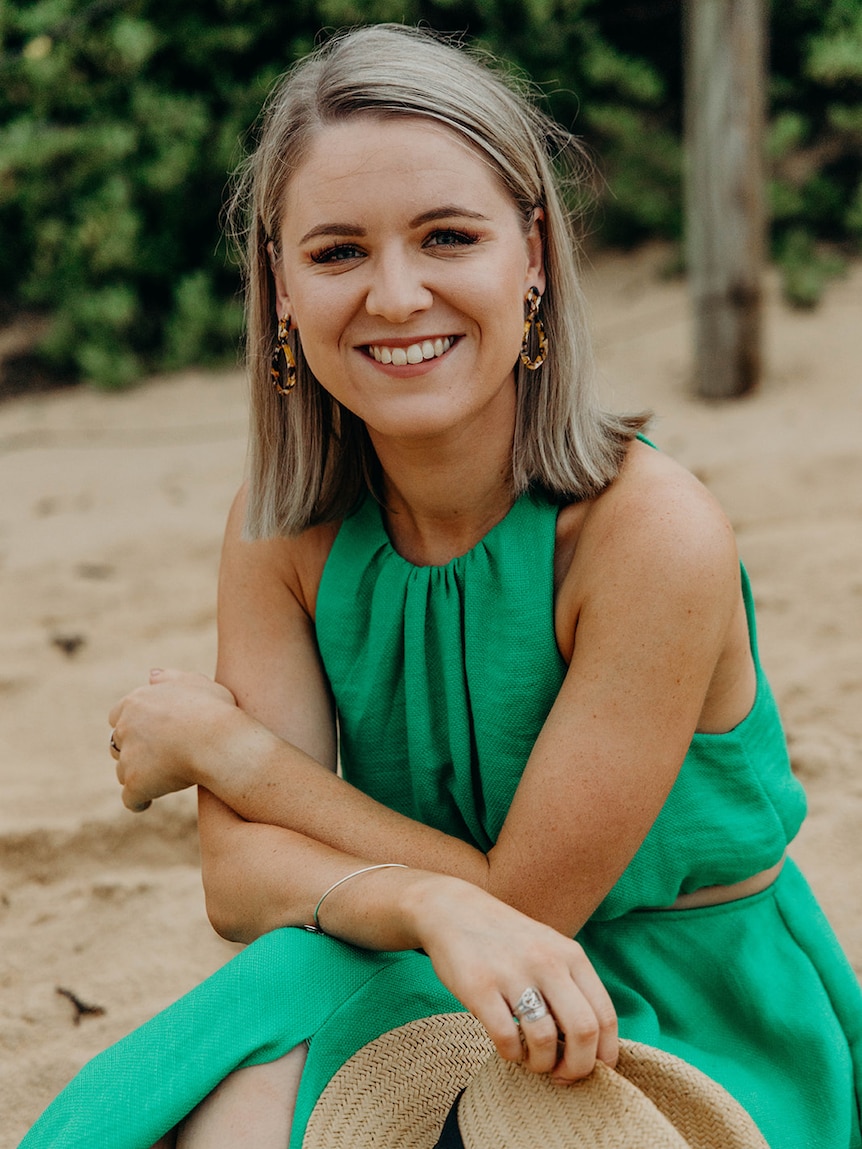 Lacinda Fisk sits outside in a green dress, holding a hat and smiling