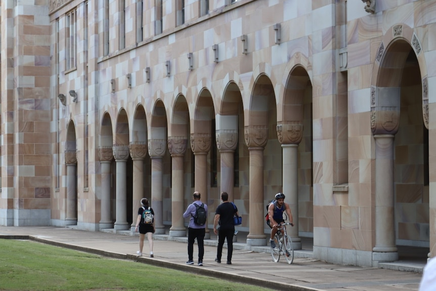 a wide image of sandstone arches at a university campus. people can be seen walking alongside the arches