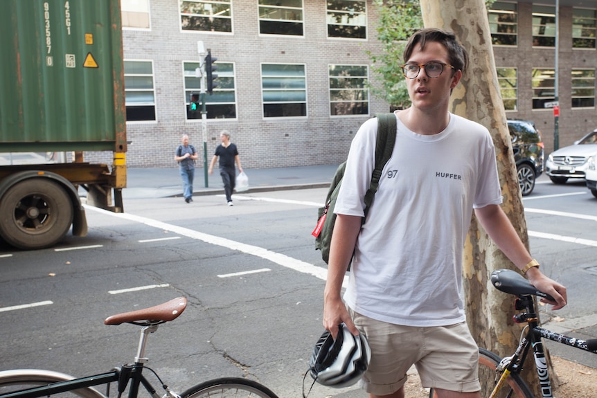 A man stands beside his bicycle beside a busy road